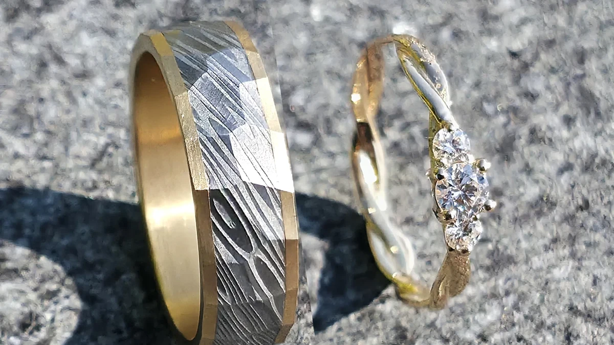 À gauche : alliance en acier damas Fraktal, intérieur et bord en or jaune, finition mate. À droite : alliance en or rose tressée, sertie d'un diamant de 3,5 mm et de deux diamants de 2,5 mm. Atelier Landès, Pouillon (Landes)